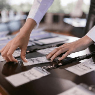 Een hand legt nekkoorden met naamkaartjes op een tafel