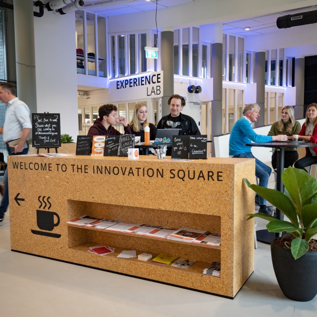 Studenten en docenten zitten samen aan statafels 