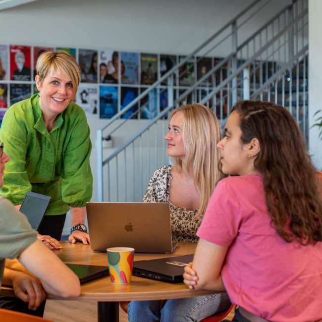 Een docent staat bij een tafel met vier studenten