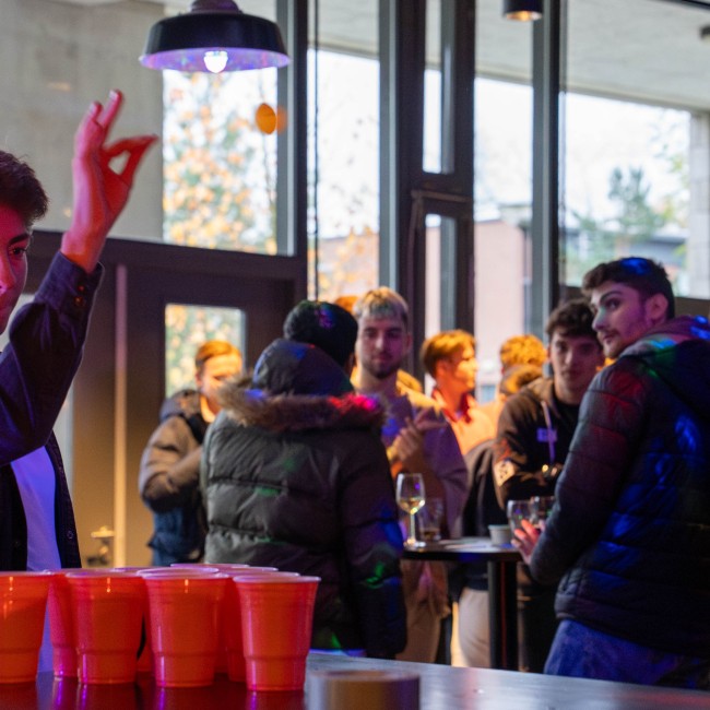Een student op een feest gooit een balletje in een beker 