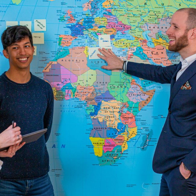 Een docent en twee studenten staan voor een wereldkaart