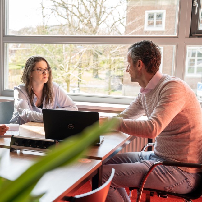 Een docent zit aan tafel met twee studenten