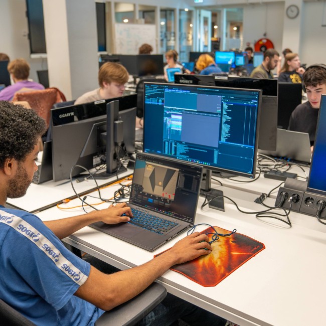 Een student werkt op een laptop in een ruimte met computers