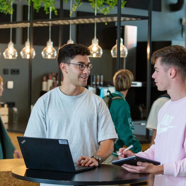 Twee studenten met een laptop aan het werk aan een statafel