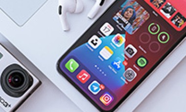 Een telefoon, laptop, camera en AirPods liggen op een tafel 