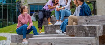 Vijf studenten zitten op houten blokken op de BUas campus