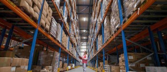 Een student staat in een magazijn met hoge stellages