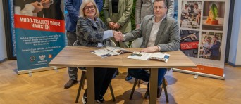 Twee mensen schudden de hand en drie staan erachter