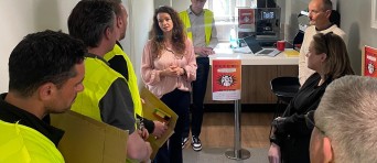 Vrouw geeft uitleg aan mannen in gele hesjes en omstanders