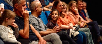 Een publiek zit op stoelen in een zaal