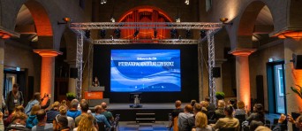 Deelnemers zitten in de zaal en wachten tot het IAC begint
