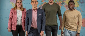 Groepsfoto van vier studenten voor een wereldkaart